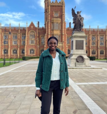 Lady in green cardigan, coat and black trousers posing in front of Queen's University Belfast
