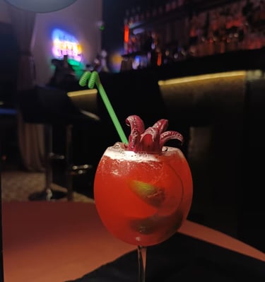Red hibiscus cocktail with lime and green straw served at a dimly lit bar.