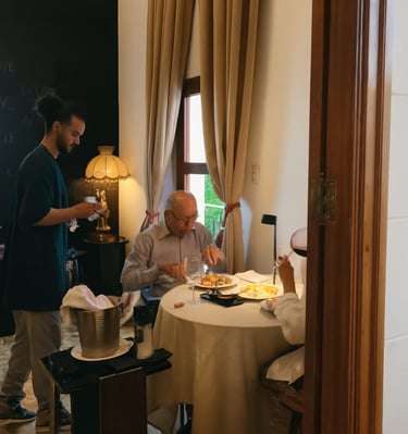 A professional waiter serving an elderly couple dining at a fine dining restaurant table.