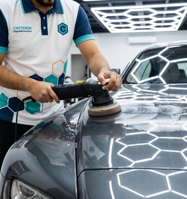 Professional car detailing specialist using a dual action polisher to buff a grey vehicle's hood.
