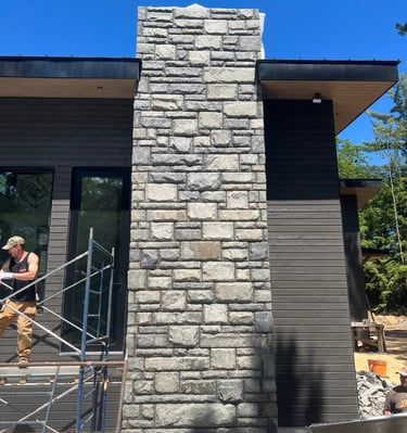 A modern home exterior featuring a natural stone veneer fireplace chimney and dark grey wood siding.