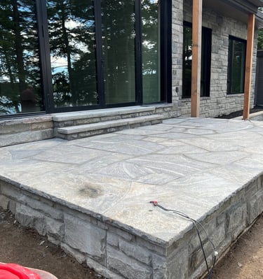 Custom granite flagstone patio and stone steps outside a modern luxury lake house.