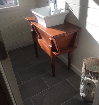 White vessel sink on a vintage wood vanity in a bathroom with dark grey floor tiles.