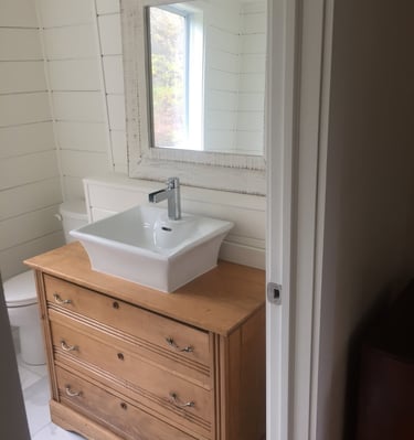 Rustic bathroom vanity featuring a wooden dresser with a white vessel sink and shiplap walls.