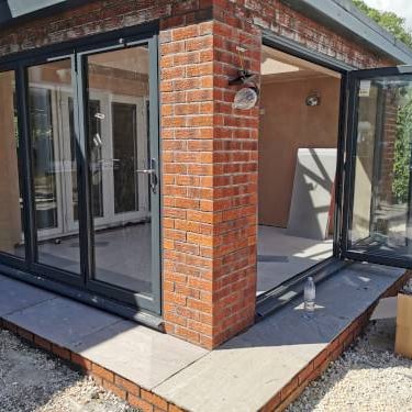 Modern anthracite grey bi-fold doors installed on a red brick home extension with stone patio.