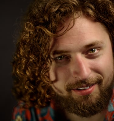 Close-up portrait of a smiling man with long curly brown hair and a beard.