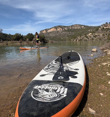 Paddle Surf en la orilla del embalse de la Toba con grandes montañas al fondo y una persona haciendo