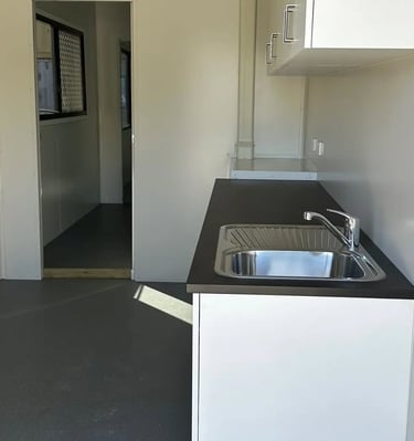 A modern kitchenette inside a portable site office cabin featuring a stainless steel sink and dark countertop.