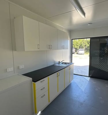 Modern portable cabin kitchenette featuring white cabinets, black countertop, and stainless steel sink.