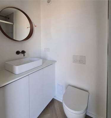 Modern minimalist bathroom with a white vessel sink, floating vanity, round mirror, and wall-hung toilet.