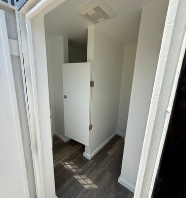 White interior restroom stall with wood-style flooring and modern door hardware.
