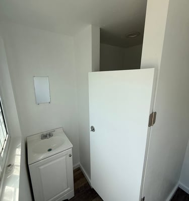 Small white bathroom vanity with a ceramic sink next to a white privacy partition door.
