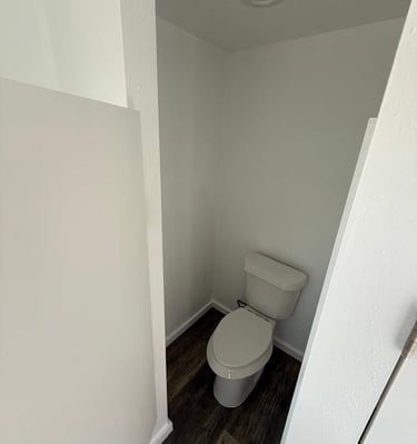 A white modern toilet installed in a small bathroom nook with dark wood-style vinyl flooring.