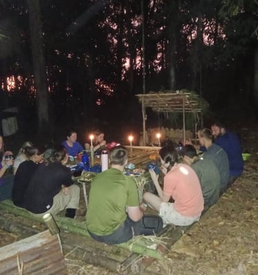 a group of people sitting around a table inside the jungle with candles