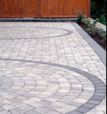 Backyard patio featuring circular stone paver designs and a dark grey border next to a wooden fence.