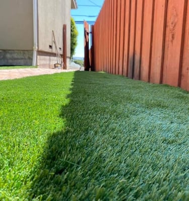 Freshly installed green artificial grass turf in a residential backyard next to a wooden fence.