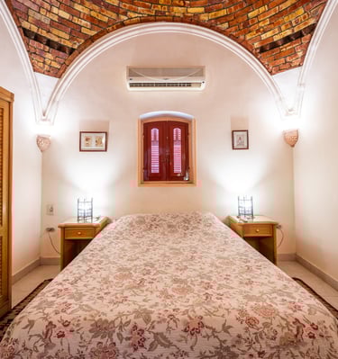 Rustic bedroom with floral bedding, wooden wardrobe, and unique vaulted brick ceiling design.