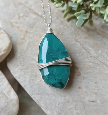 Close-up of a delicate wire-wrapped crystal pendant resting on driftwood with soft natural light.