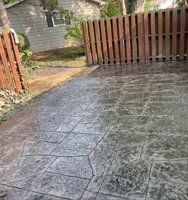 Custom decorative stamped concrete patio with slate texture and brown wooden privacy fence.