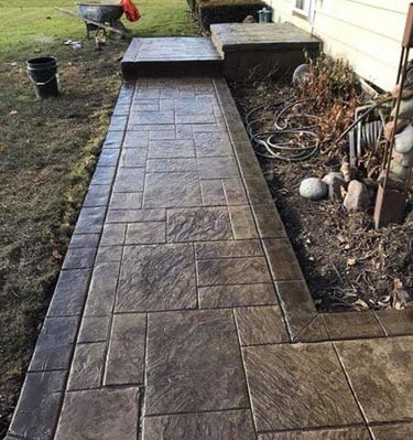 Custom dark brown stamped concrete walkway with a slate pattern leading to a home entrance.