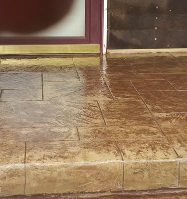 Custom brown stamped concrete patio entryway with a gloss finish and textured stone pattern.