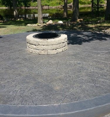 Circular stamped concrete patio with a stone fire pit near a backyard river.