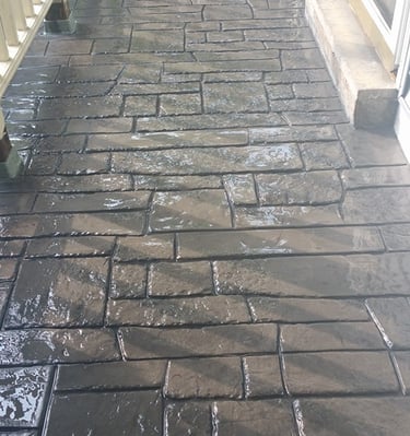 Freshly sealed grey stamped concrete patio with a decorative flagstone pattern and glossy finish.