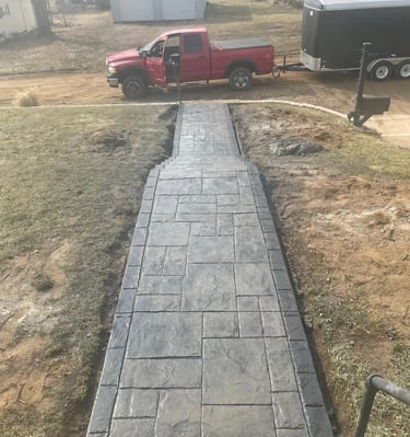 Custom stamped concrete walkway with a dark grey ashlar slate pattern leading to a residential driveway.