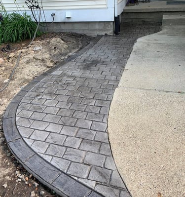 Curved grey stamped concrete walkway with a brick pattern leading to a residential front porch.