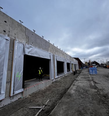 Construction worker standing at a commercial building site with concrete walls and window openings.