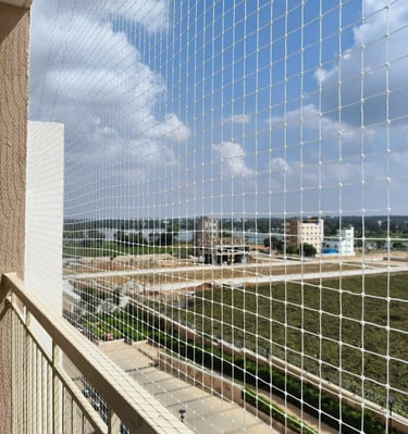 Wide-angle view showing a balcony fully enclosed with safety nets, overlooking a bustling Thane East