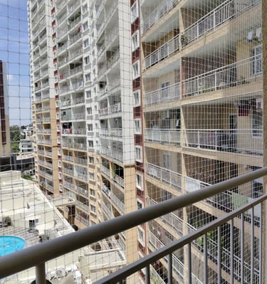 Technician carefully fitting a safety net frame on a balcony railing under bright daylight.