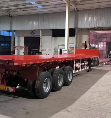 Red 3-axle flatbed semi-trailer parked in our industrial manufacturing warehouse facility.