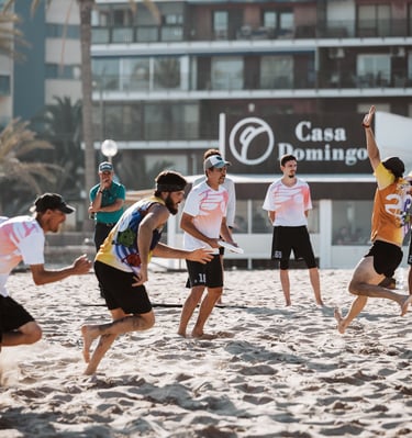 Fotografía de dos equipos compitiendo en un partido de ultimate frisbee en una playa de día