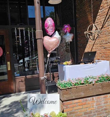 A DJ setup in front of a bridal shop with flowers, balloons and a welcome sign