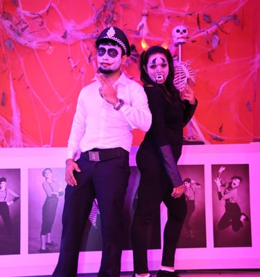 A couple in Halloween costumes and skull face paint posing in front of a spooky spiderweb backdrop.
