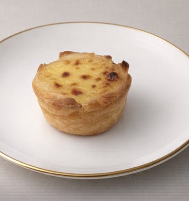 Golden Portuguese custard tart with caramelized top on a white gold-rimmed plate.