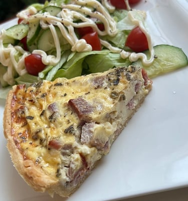 A slice of homemade quiche lorraine served with a fresh garden salad on a white plate.