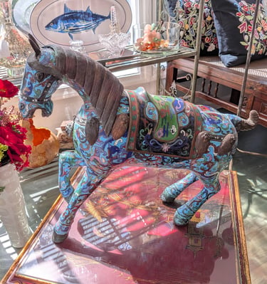 Ornate blue cloisonne horse statue with intricate floral patterns displayed in a sunlit antique shop.