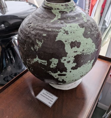 Large globular stoneware vessel with a distressed celadon glaze on a wooden table.