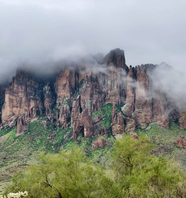 Misty fog rolling over the jagged peaks of the Superstition Mountains in Arizona's desert landscape.