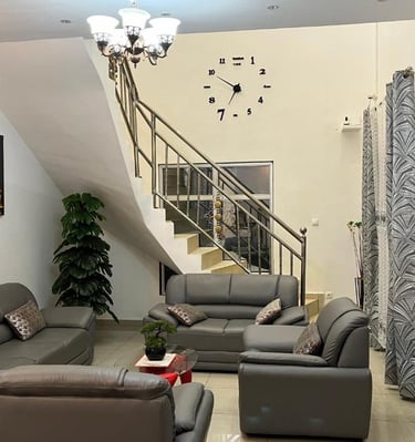 Modern living room with grey leather sofas, a staircase with metal railings, and a large decorative wall clock.