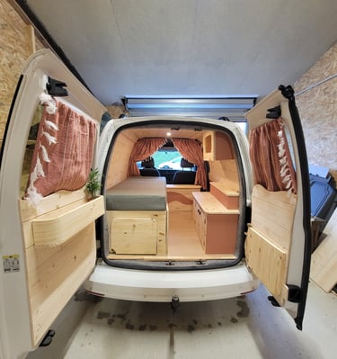 Aménagement complet d'un fourgon blanc en bois clair avec rideaux terracotta et lit peigne, réalisé