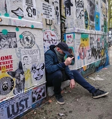 Dacarter in a mask and cap sitting against a wall in Star Yard Brick Lane