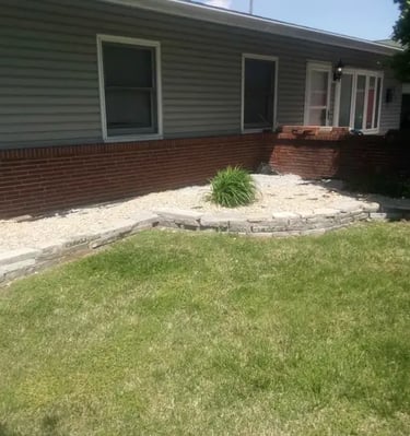 Backyard landscape featuring a tiered stone retaining wall and decorative gravel garden bed.