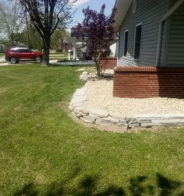 Residential landscaping featuring a low natural stone retaining wall and decorative gravel bed.