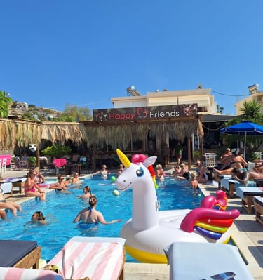 Crowded outdoor swimming pool at a resort with people relaxing and a large inflatable unicorn float.