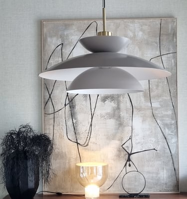 Modern grey tiered pendant light hanging above a buffet with abstract art and a glowing glass table lamp.