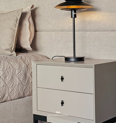 Modern beige nightstand with black handles and a sleek black metal lamp in a cozy bedroom setting.