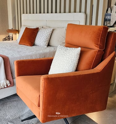 Poltrona moderna de veludo laranja com uma almofada branca num quarto com decoração elegante.